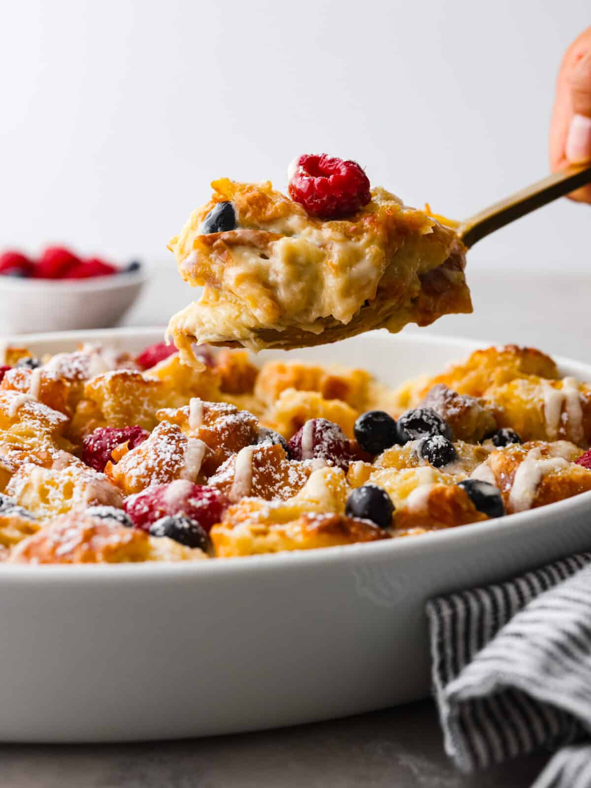 If you love sweet breakfasts, you're in for a treat. This croissant breakfast casserole features tender croissant pieces and fresh berries all coated in a cream cheese custard. As if that's not good enough, everything is topped off with a homemade lemon glaze that's absolutely heavenly. It's love at first bite! Serving a scoop of croissant breakfast casserole.