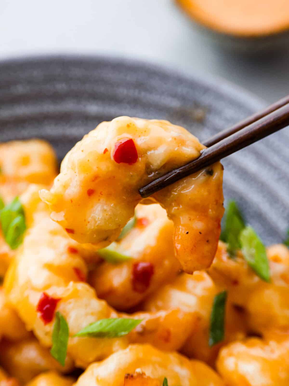 Shake up dinnertime with this dynamite shrimp! Itโs fried to golden-brown, crispy perfection and tossed in a creamy, spicy sauce. Your family will be begging for seconds! Picking up a piece of shrimp with chopsticks.