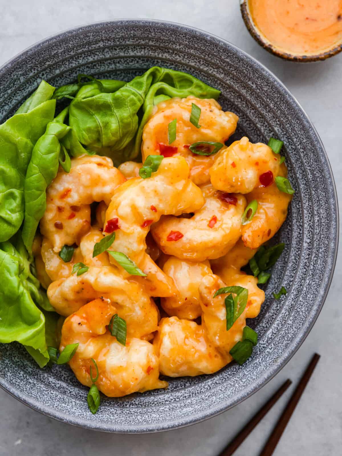Shake up dinnertime with this dynamite shrimp! Itโs fried to golden-brown, crispy perfection and tossed in a creamy, spicy sauce. Your family will be begging for seconds! Top-down view of dynamite shrimp served in a stoneware bowl with greens.