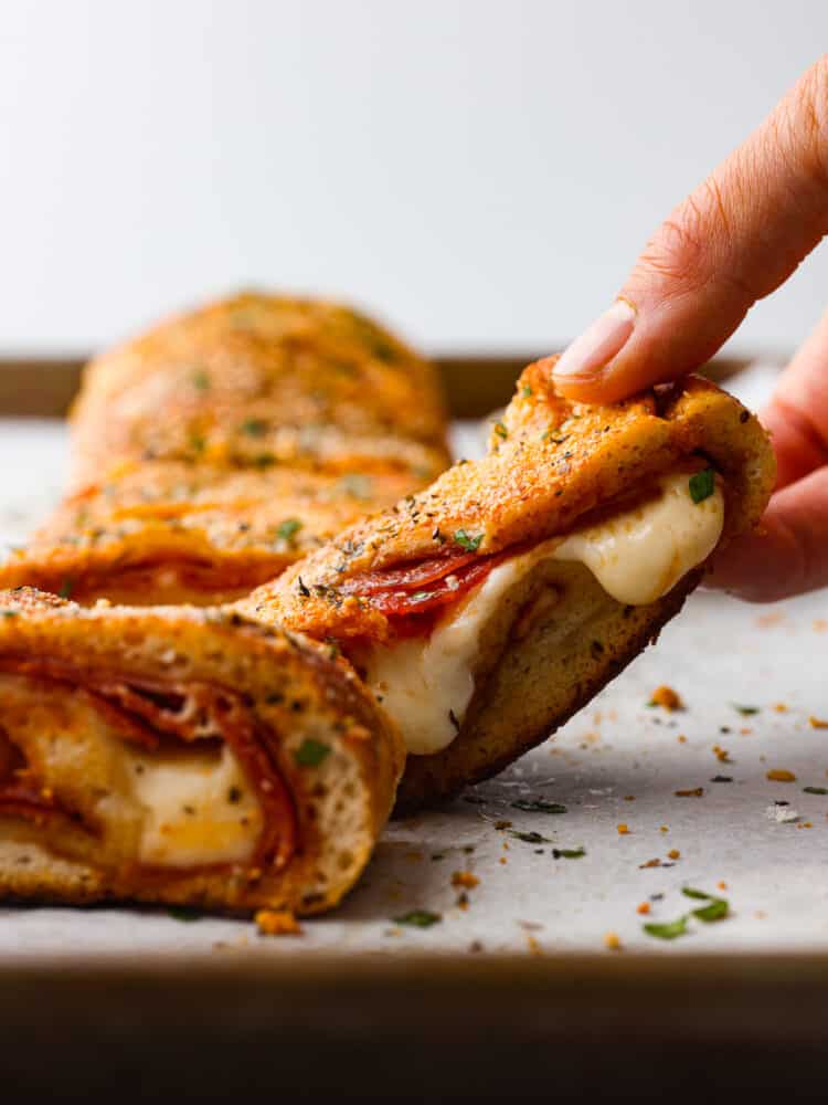 This quick and easy Stromboli gets loaded with Italian salami, pepperoni, pizza sauce and cheese. It's so quick, easy and delicious you will want to make it again and again! A slice being picked up.