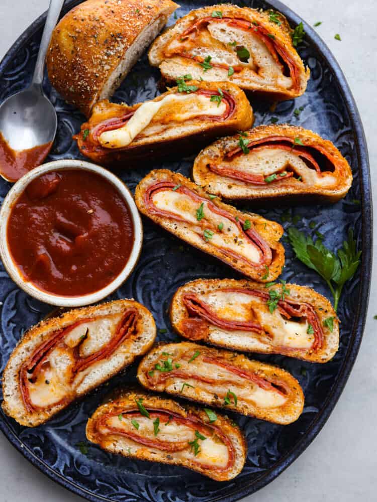 This quick and easy Stromboli gets loaded with Italian salami, pepperoni, pizza sauce and cheese. It's so quick, easy and delicious you will want to make it again and again! Sliced stromboli served on a blue plate with pizza sauce for dipping.