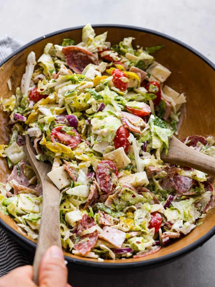 It’s like your favorite deli sub ditched the bread and got a glow-up. Think layers of crispy lettuce, your favorite meats, and a creamy dressing all in this yummy Grinder Salad form! Grinder salad being tossed with 2 wooden spoons.