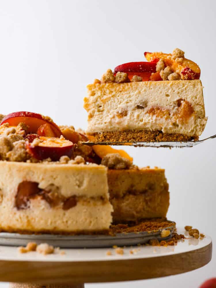 Indulge in a delightful treat with this mouthwatering Peach Cobbler Cheesecake recipe. A delicious combination of creamy cheesecake, caramelized peaches, and a buttery streusel crust, all perfectly balanced to create a dessert that will impress any crowd! The side view of a slice of peach cobbler cheesecake being taken out with a pie server.