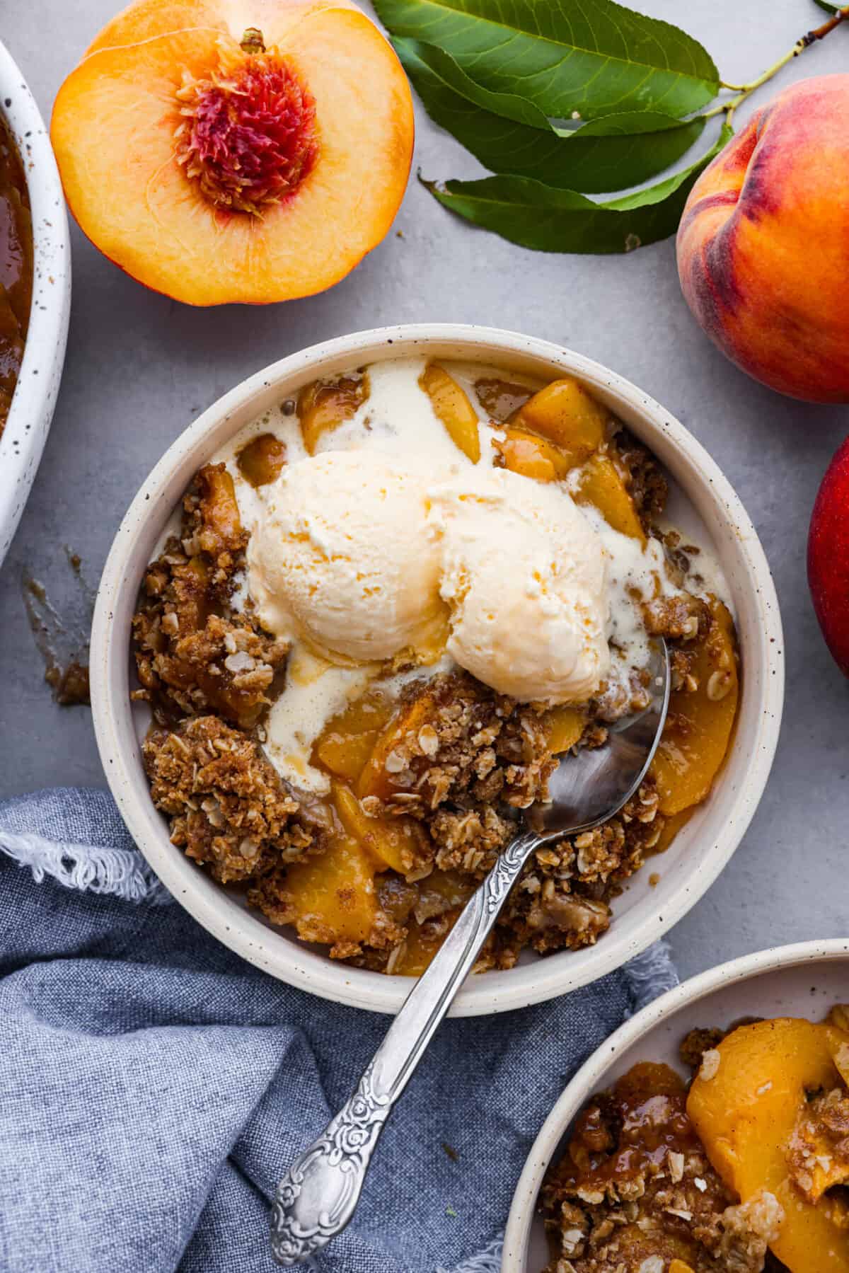 Celebrate summer with a mouthwatering Peach Crisp! Juicy peaches, sweet cinnamon, and a crunchy topping come together for a delightful treat that's perfect when it's served warm with a scoop of vanilla ice cream! The top view of a bowl of peach crisp with a scoop of vanilla ice cream on top.