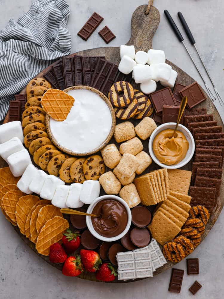 Just in time for summer barbecues and camping trips, this s'mores charcuterie board is here to sweeten things up! It features a mix of different types of chocolate, crackers, marshmallows, and spreads so everyone in your family can create their own perfect sweet treat. A whole sโmores charcuterie board made with various types of chocolate, marshmallows, and sweet spreads.