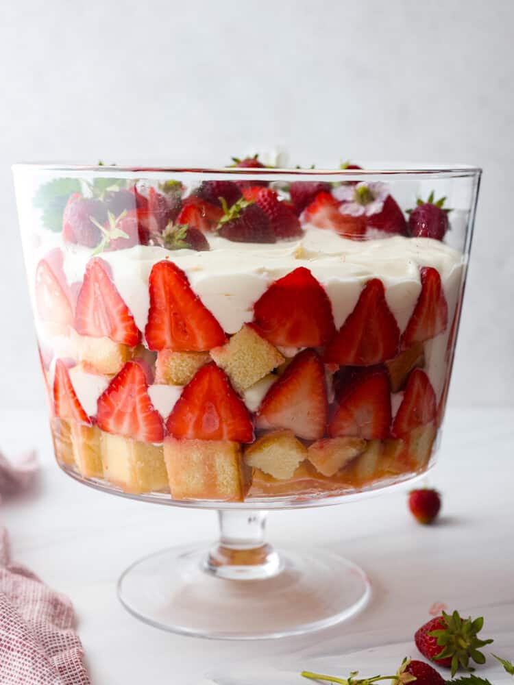 Get ready to dig into this amazing strawberry trifle! Layers of juicy strawberries, creamy cheesecake, and fluffy pound cake come together to create the ultimate summer dessert! Hero image of strawberry trifle. All of the layers can be seen through the glass dish.