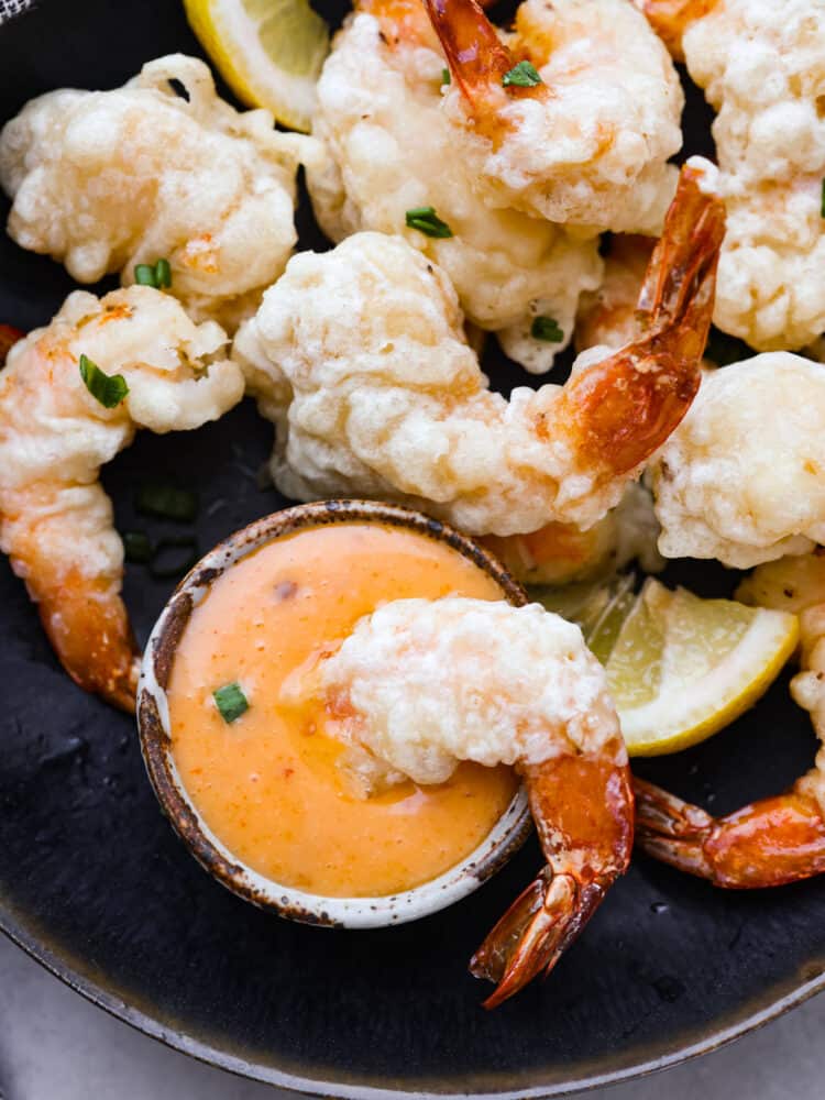 Lightly battered and fried to golden perfection, this shrimp tempura is the perfect dish for any seafood lover! One bite of its crispy goodness and you'll be hooked. A piece of shrimp being dipped in the sauce.