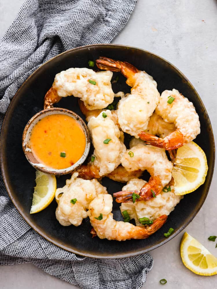 Lightly battered and fried to golden perfection, this shrimp tempura is the perfect dish for any seafood lover! One bite of its crispy goodness and you'll be hooked. Shrimp tempura served in a brown bowl with a small cup of sriracha mayo.