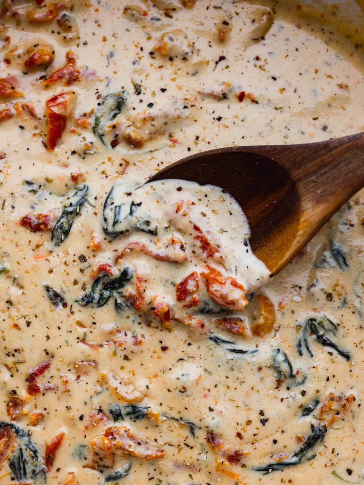 Creamy Tuscan garlic sauce is the secret weapon you didn't know your kitchen needed โ it makes all of your favorite meals unforgettable! It's the most amazing blend of sun-dried tomatoes, cream, garlic, parmesan, and tasty seasonings. Whether it's pasta, meat, or fish, this sauce does it all! Mixing creamy Tuscan garlic sauce with a wooden spoon.