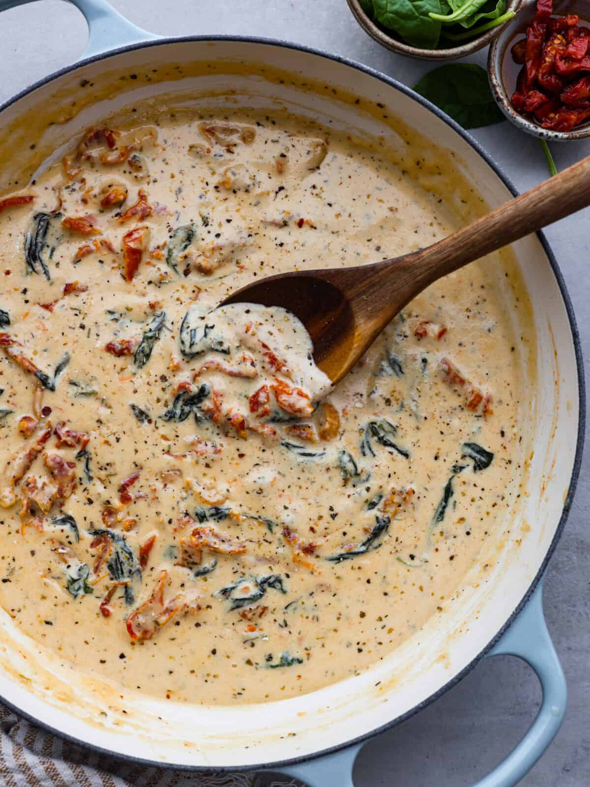 Creamy Tuscan garlic sauce is the secret weapon you didn't know your kitchen needed โ it makes all of your favorite meals unforgettable! It's the most amazing blend of sun-dried tomatoes, cream, garlic, parmesan, and tasty seasonings. Whether it's pasta, meat, or fish, this sauce does it all! Tuscan garlic sauce in a blue and white saucepan.