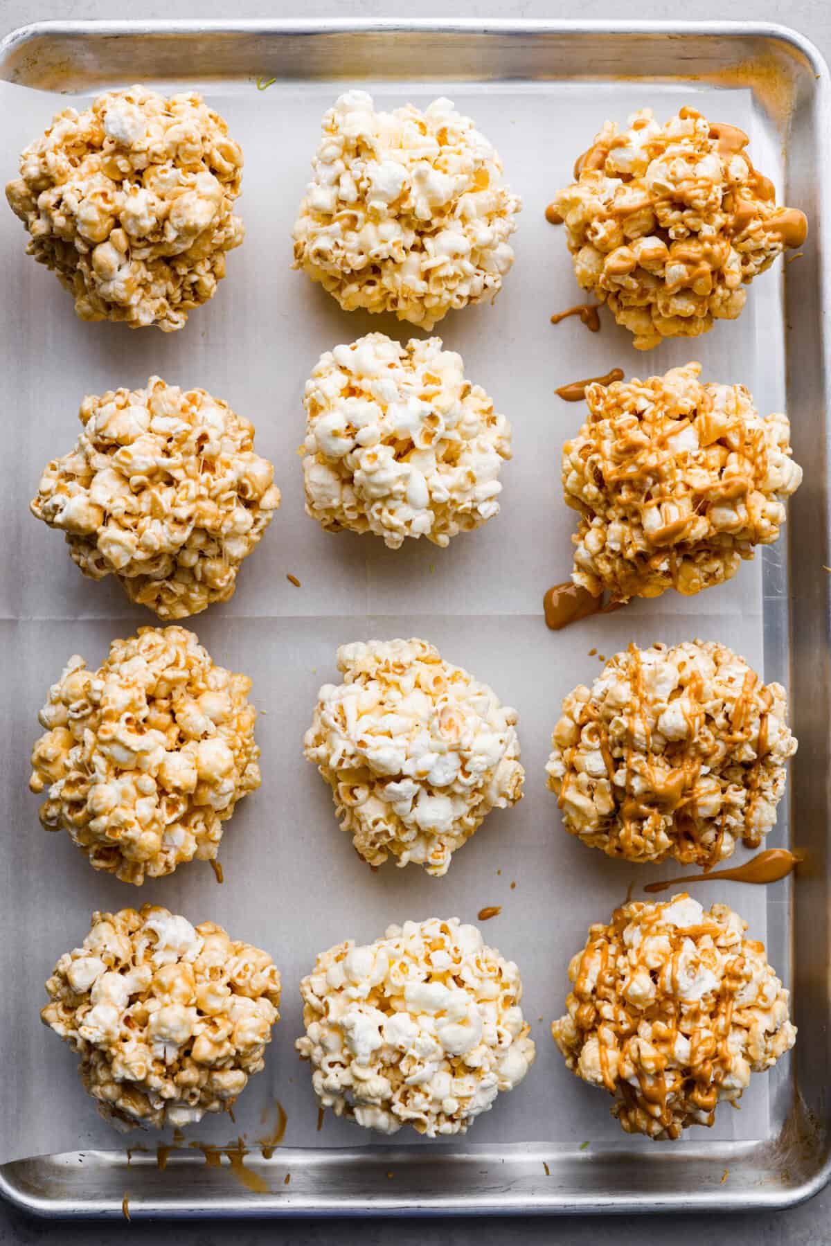 These popcorn balls are a tasty snack that will win the hearts of kids and adults alike! This recipe has 3 different flavors, marshmallow, peanut butter, and caramel, so there's something for everyone! You're going to love each soft and buttery bite. Top-down view of the popcorn balls on a parchment paper-lined baking sheet.