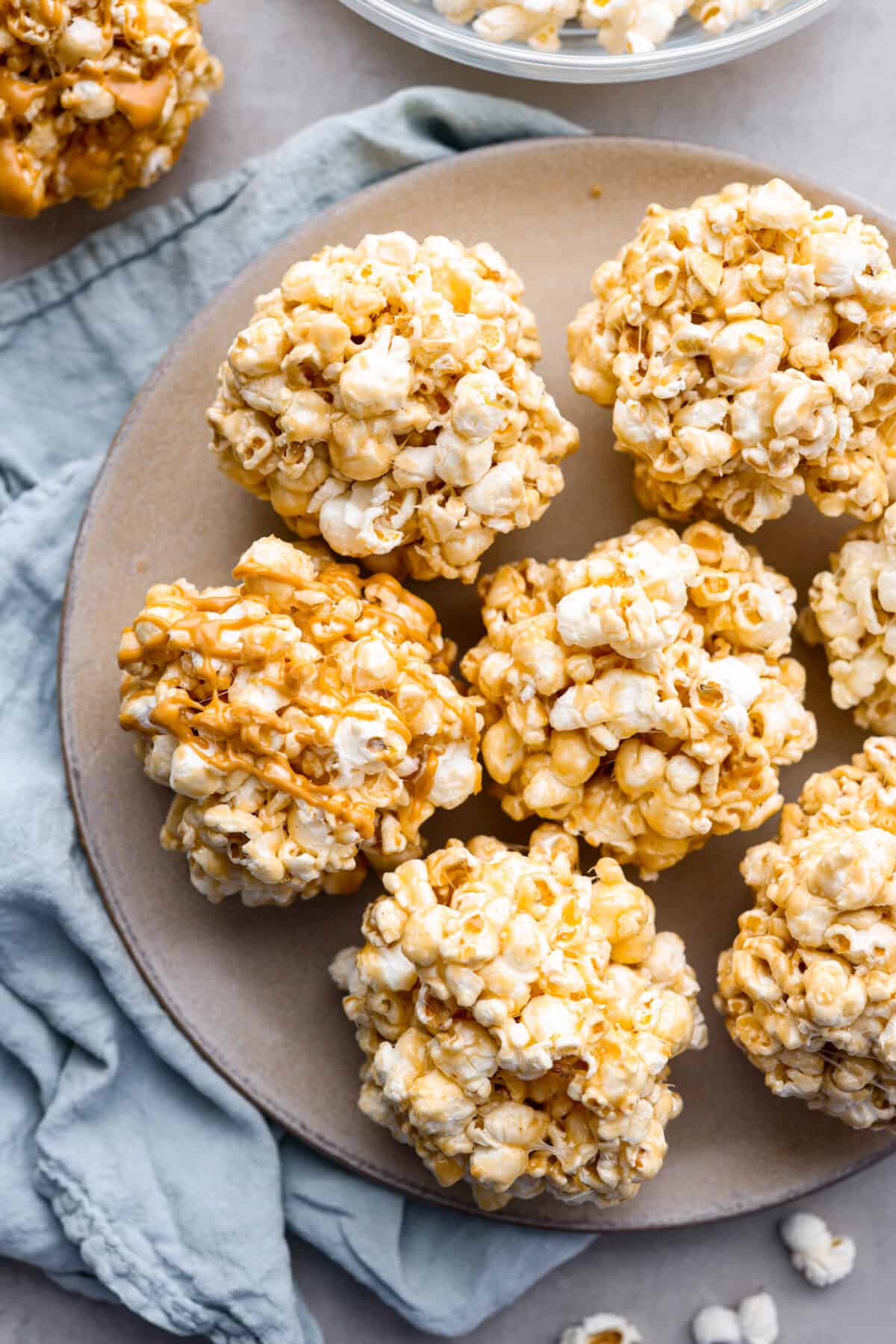 These popcorn balls are a tasty snack that will win the hearts of kids and adults alike! This recipe has 3 different flavors, marshmallow, peanut butter, and caramel, so there's something for everyone! You're going to love each soft and buttery bite. Marshmallow, caramel, and peanut butter popcorn balls on a gray plate.