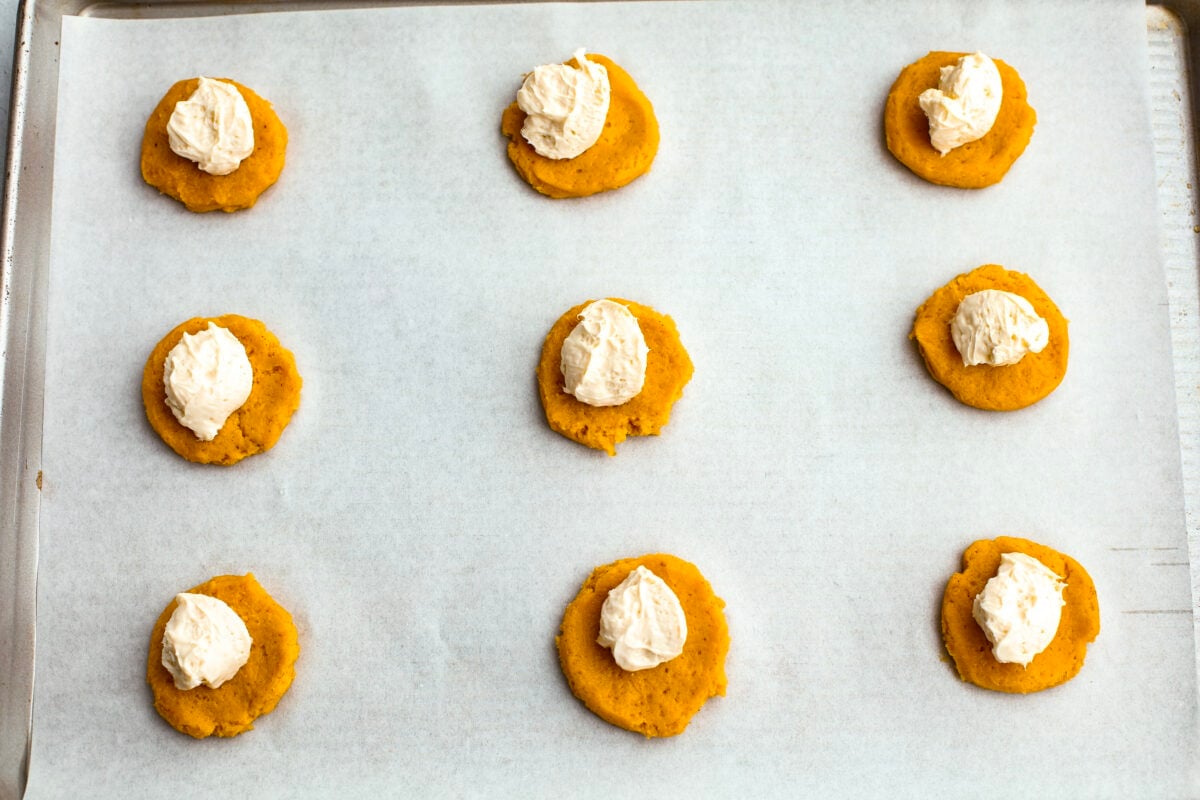 Pumpkin cheesecake snickerdoodle dough balls flattened with cream cheese on a baking sheet with parchment paper.