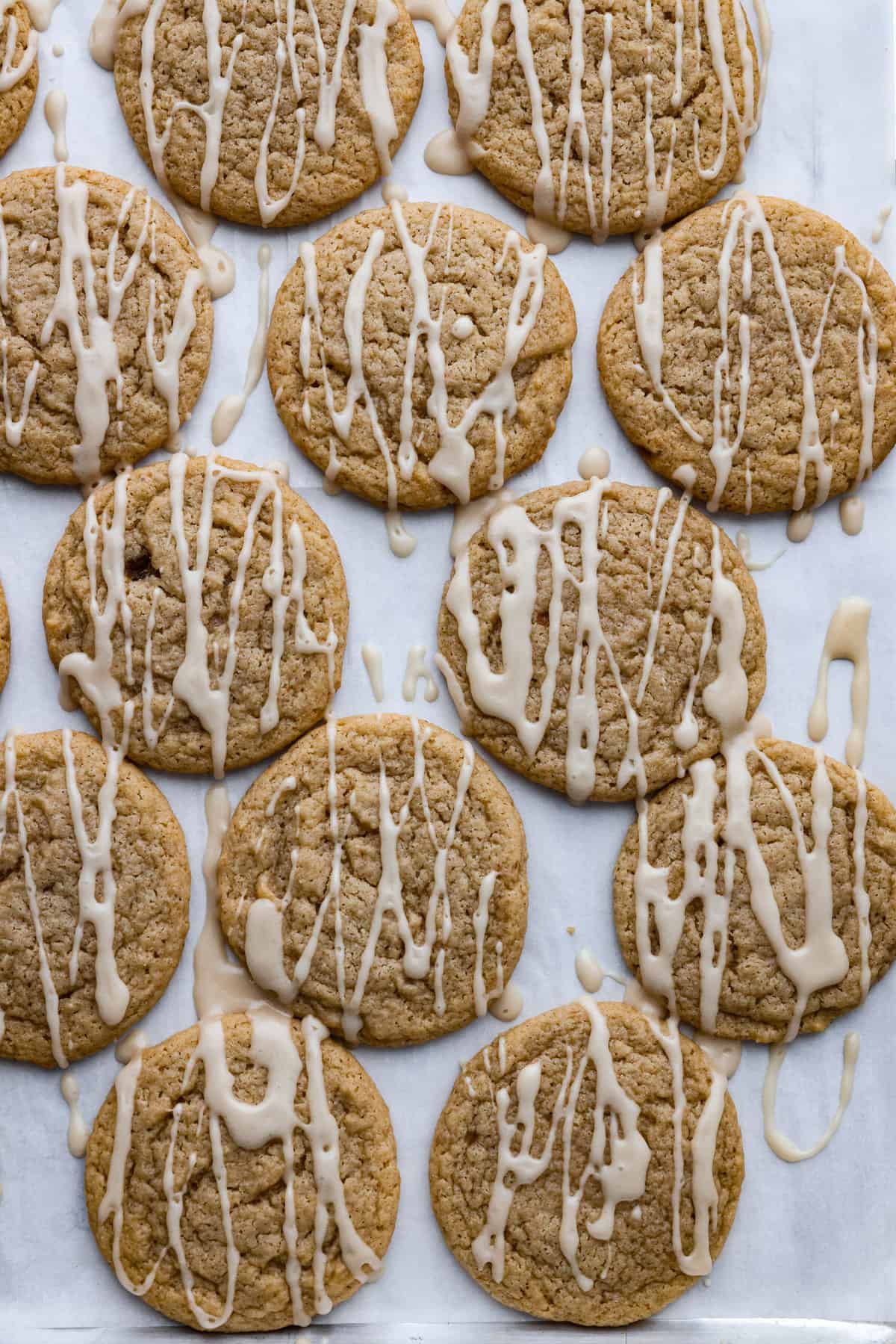 These soft and delicious Apple Cider Cookies are a delightful blend of apple cider, warm spices, and drizzled with a sweet glaze. These cookies are a cozy and irresistible treat that's perfect for any occasion. Apple cider cookies on parchment paper drizzled with a white glaze.