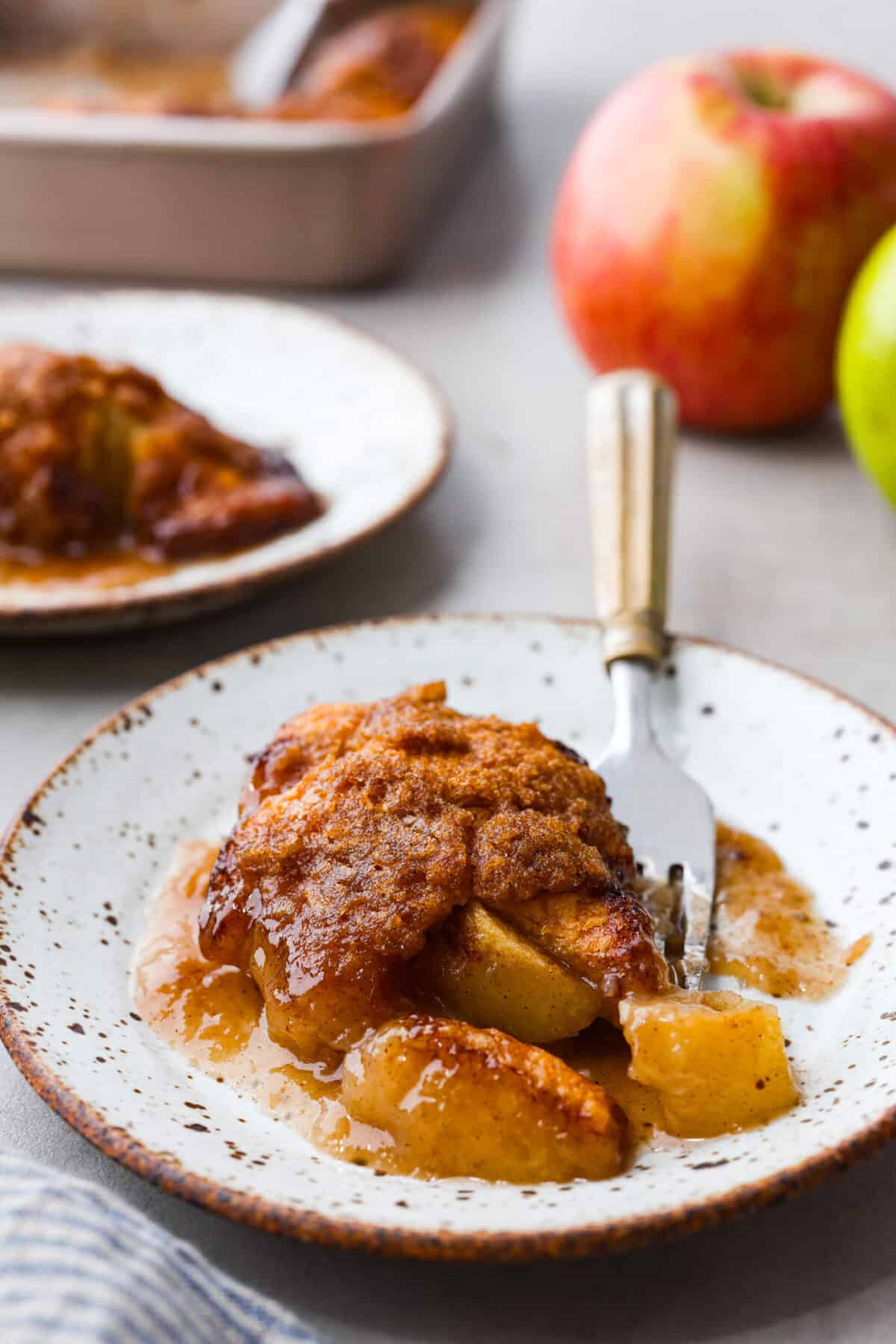 This semi-homemade version of apple dumplings is made with a delicious surprise ingredient! Apple slices get wrapped in crescent dough, smothered in a caramel sauce, then topped with bubbly canned Sprite. You won't believe how incredible this concoction is when it bakes up! Baked apple dumplings on a white speckled plate with a fork.