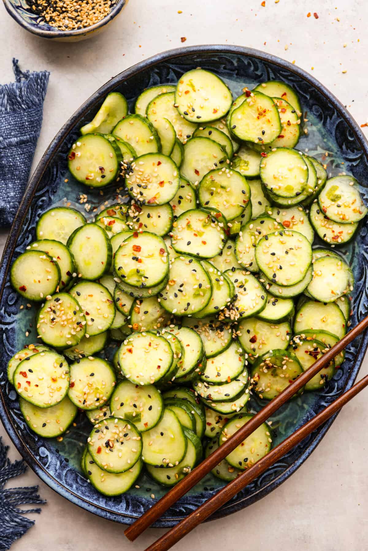 This delightful Asian Cucumber Salad is a blend of flavors creating a refreshing dish that's finished with a sprinkle of red pepper flakes and sesame seeds. It makes the perfect snack or side dish to complement any meal. A platter of Asian Cucumber Salad with a pair of chopsticks on the side.
