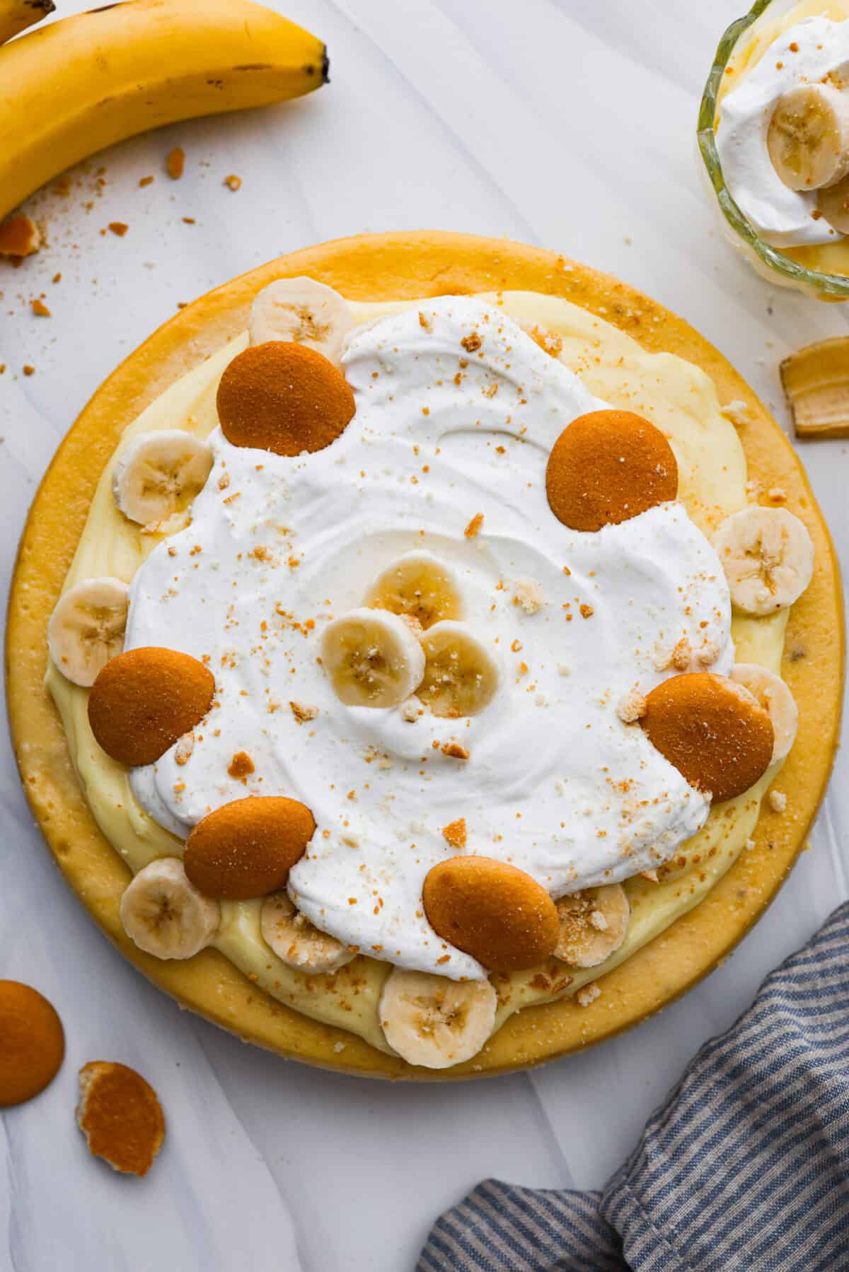 Get ready to enjoy a slice of pure dessert perfection with this Banana Pudding Cheesecake recipe. This yummy dessert has a buttery vanilla wafer crust, a velvety cream cheese filling with ripe bananas, and a classic banana pudding topping. The top view of a banana pudding cheesecake that is topped with sliced bananas and Nilla wafers.