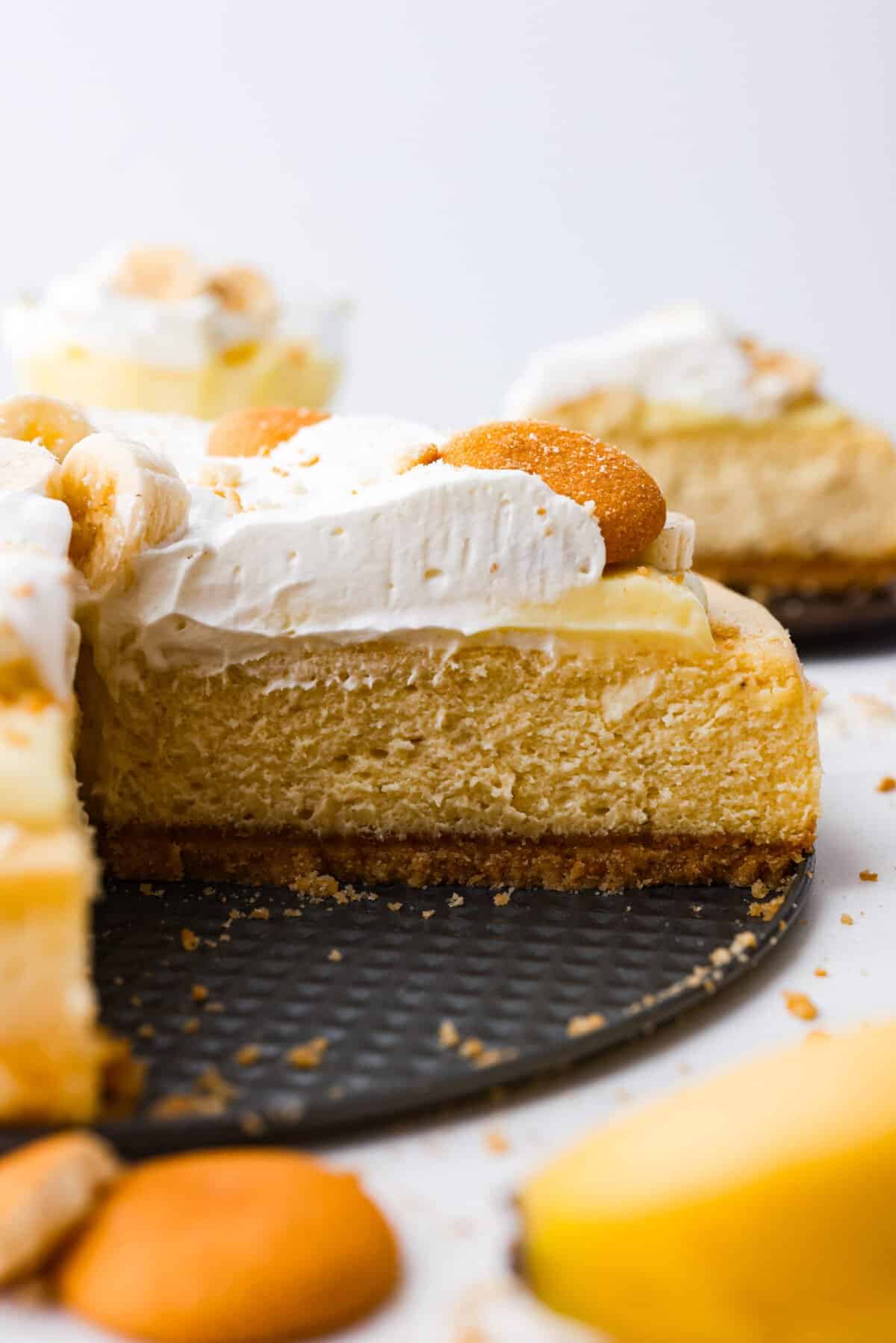 Get ready to enjoy a slice of pure dessert perfection with this Banana Pudding Cheesecake recipe. This yummy dessert has a buttery vanilla wafer crust, a velvety cream cheese filling with ripe bananas, and a classic banana pudding topping. The side view of a slice of banana pudding cheesecake.