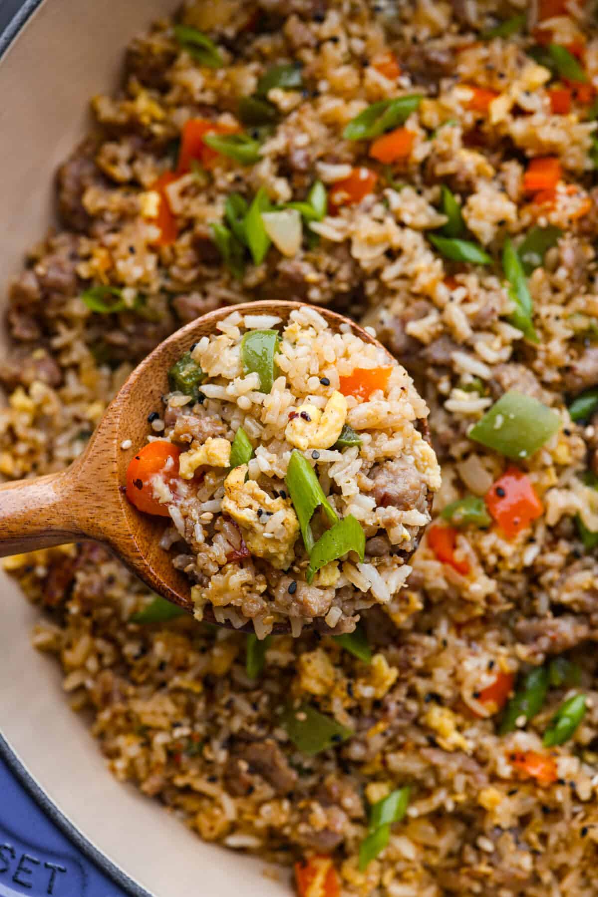 Upgrade your breakfast with this simple Breakfast Fried Rice. Sausage, eggs, and colorful bell peppers mix with white rice, all seasoned for a tasty kick. Top it off with green onions and everything bagel seasoning. A closeup of a spoonful or fried rice on a wooden spoon.