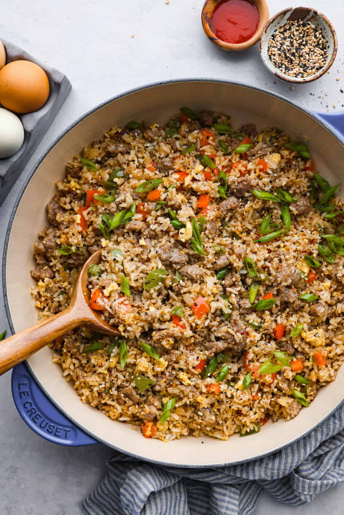 Upgrade your breakfast with this simple Breakfast Fried Rice. Sausage, eggs, and colorful bell peppers mix with white rice, all seasoned for a tasty kick. Top it off with green onions and everything bagel seasoning. A pan of breakfast fried rice with a wooden spoon.