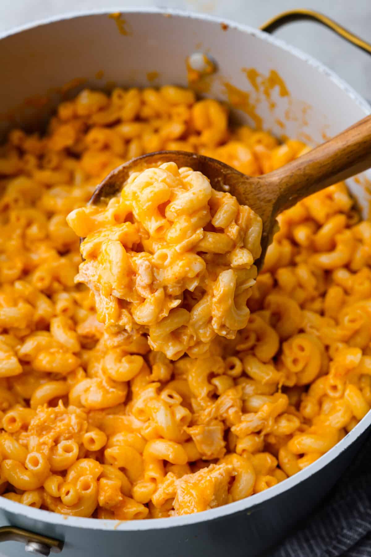 Mac and cheese gets a makeover with the addition of intense buffalo flavor! It's loaded with chicken and tender macaroni then tossed in a creamy cheese sauce. You will love this tasty version of buffalo chicken mac and cheese. Close view of buffalo chicken mac and cheese cooked in a large pot with a wood spoon lifting up macaroni.