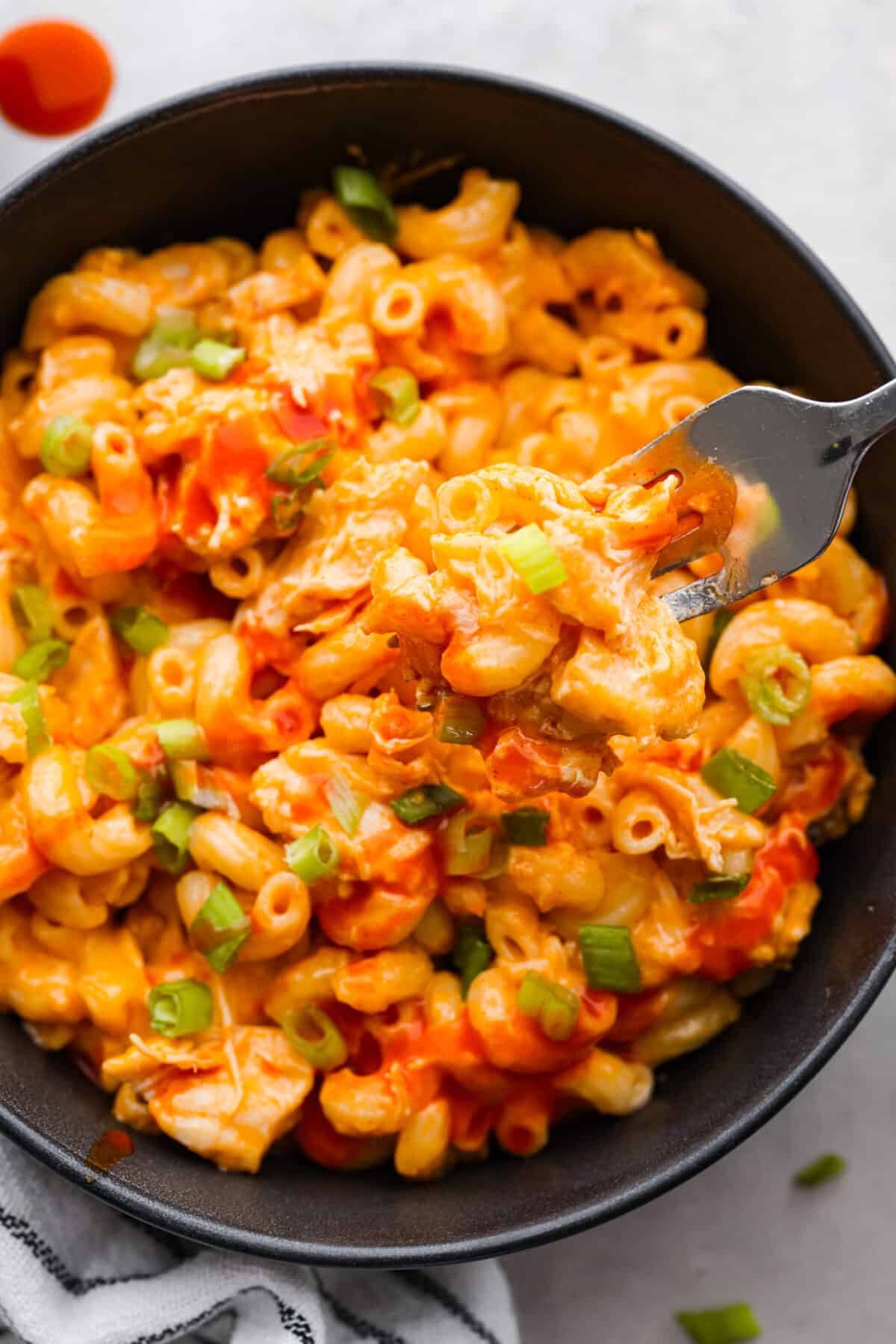 Mac and cheese gets a makeover with the addition of intense buffalo flavor! It's loaded with chicken and tender macaroni then tossed in a creamy cheese sauce. You will love this tasty version of buffalo chicken mac and cheese. Close view of buffalo chicken mac and cheese in a black bowl with a silver fork lifting up macaroni.