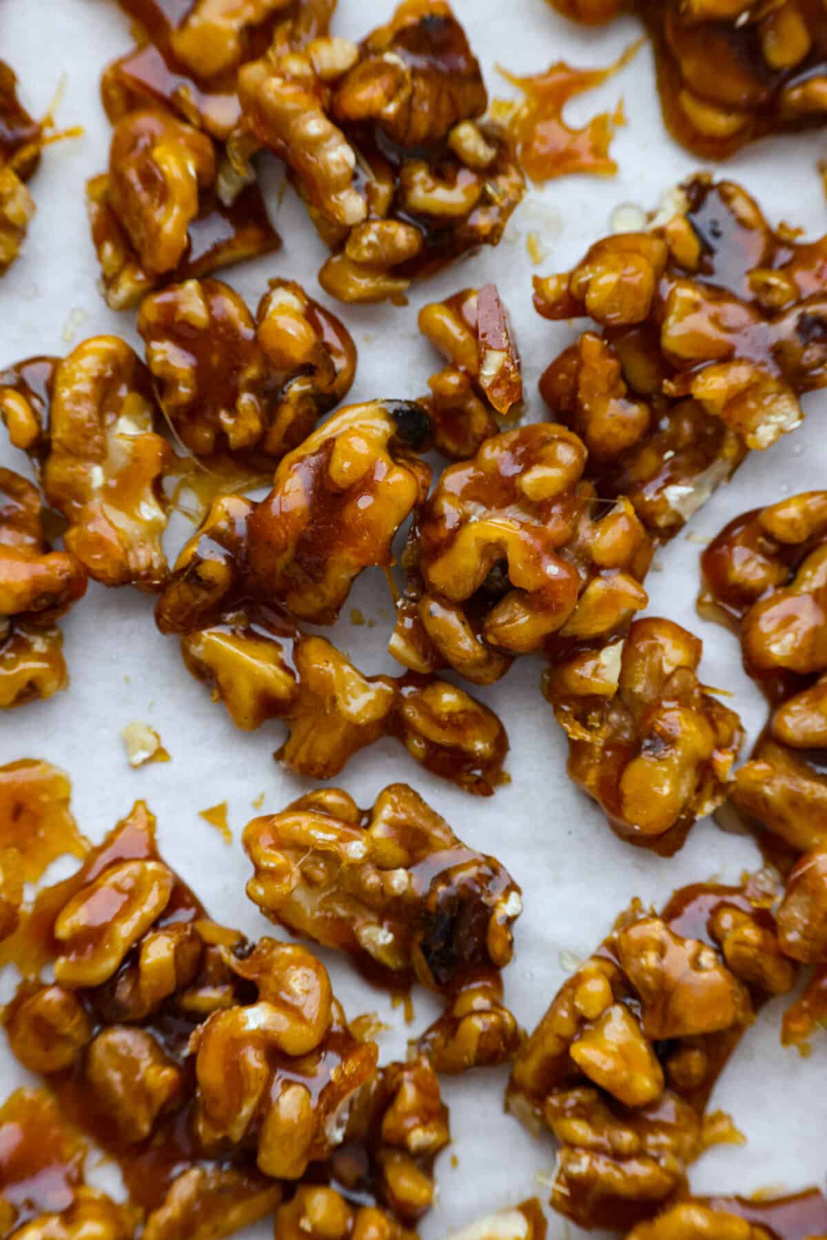 Elevate your food with these easy Candied Walnuts. With just sugar and walnut halves, these are a sweet and crunchy treat perfect for salads, desserts, or on their own as a delicious snack! A close up of candied walnuts on parchment paper.
