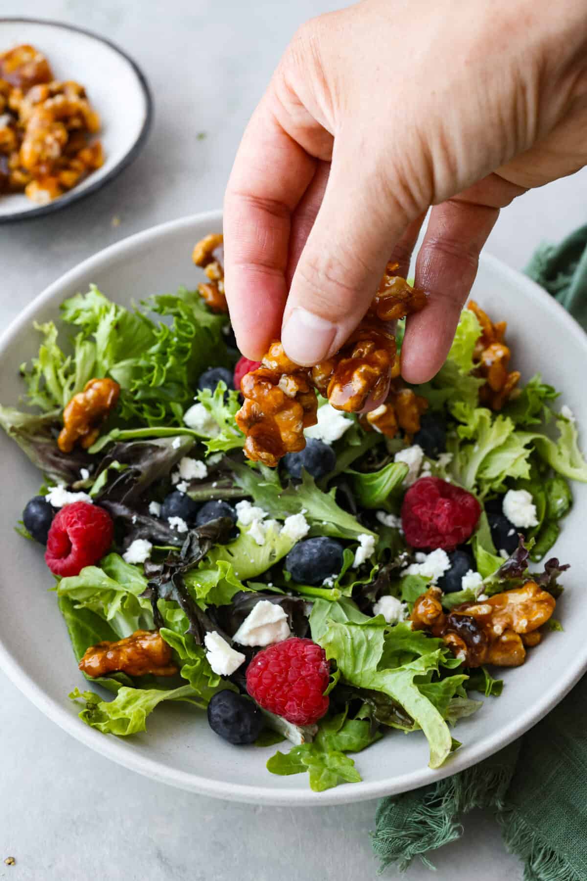 Elevate your food with these easy Candied Walnuts. With just sugar and walnut halves, these are a sweet and crunchy treat perfect for salads, desserts, or on their own as a delicious snack! A salad being sprinkled with candied walnuts.