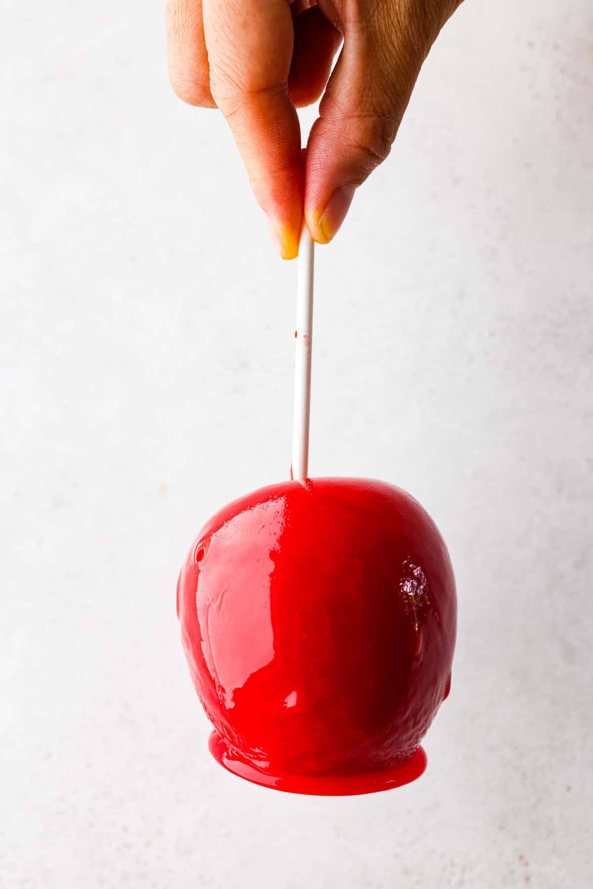 Fall is here, and that means itโs time to make a tasty batch of candy apples! Your favorite crisp apples coated in a glossy, red sugar mixture that almost looks too good to eat! A whole candied apple being picked up by the stick.
