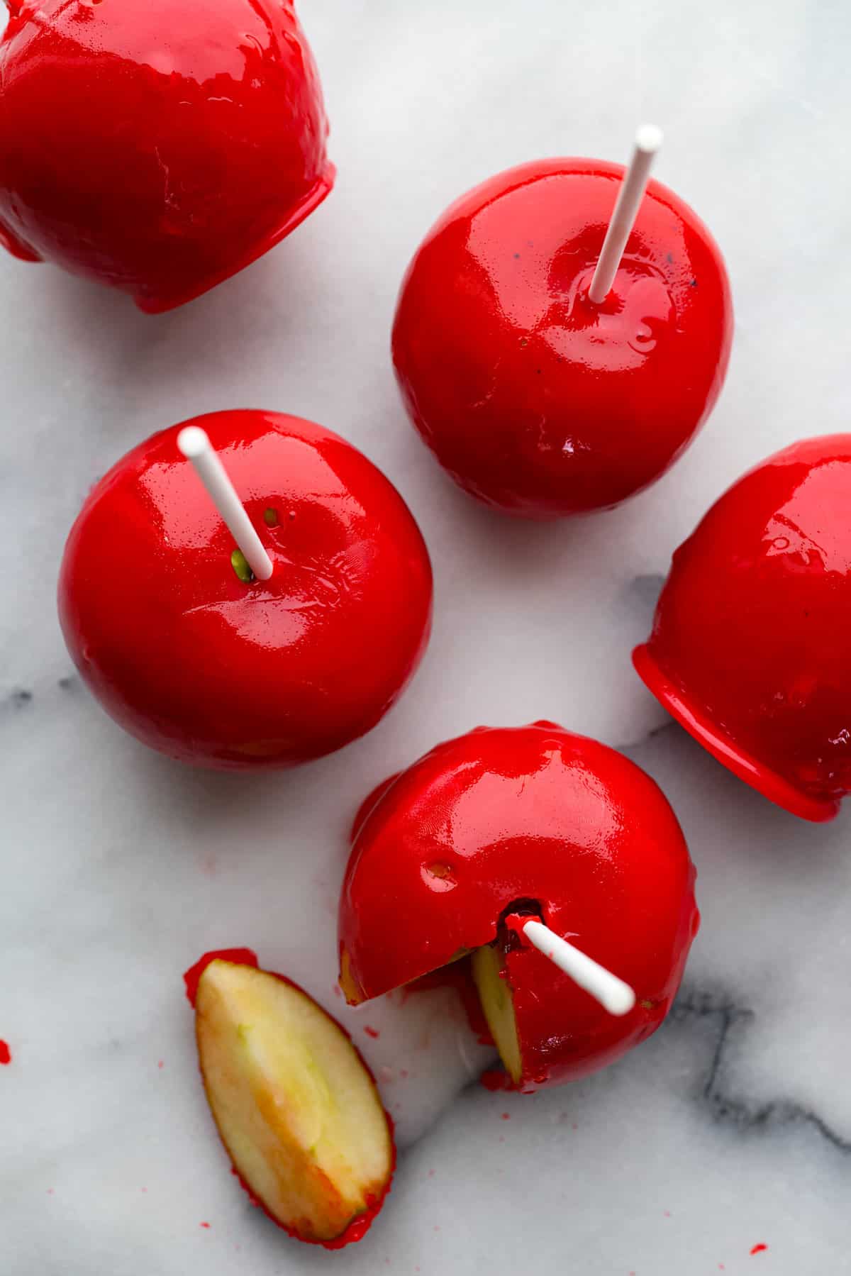 Fall is here, and that means itโs time to make a tasty batch of candy apples! Your favorite crisp apples coated in a glossy, red sugar mixture that almost looks too good to eat! Top-down view of candy apples. One has a piece cut out of it.