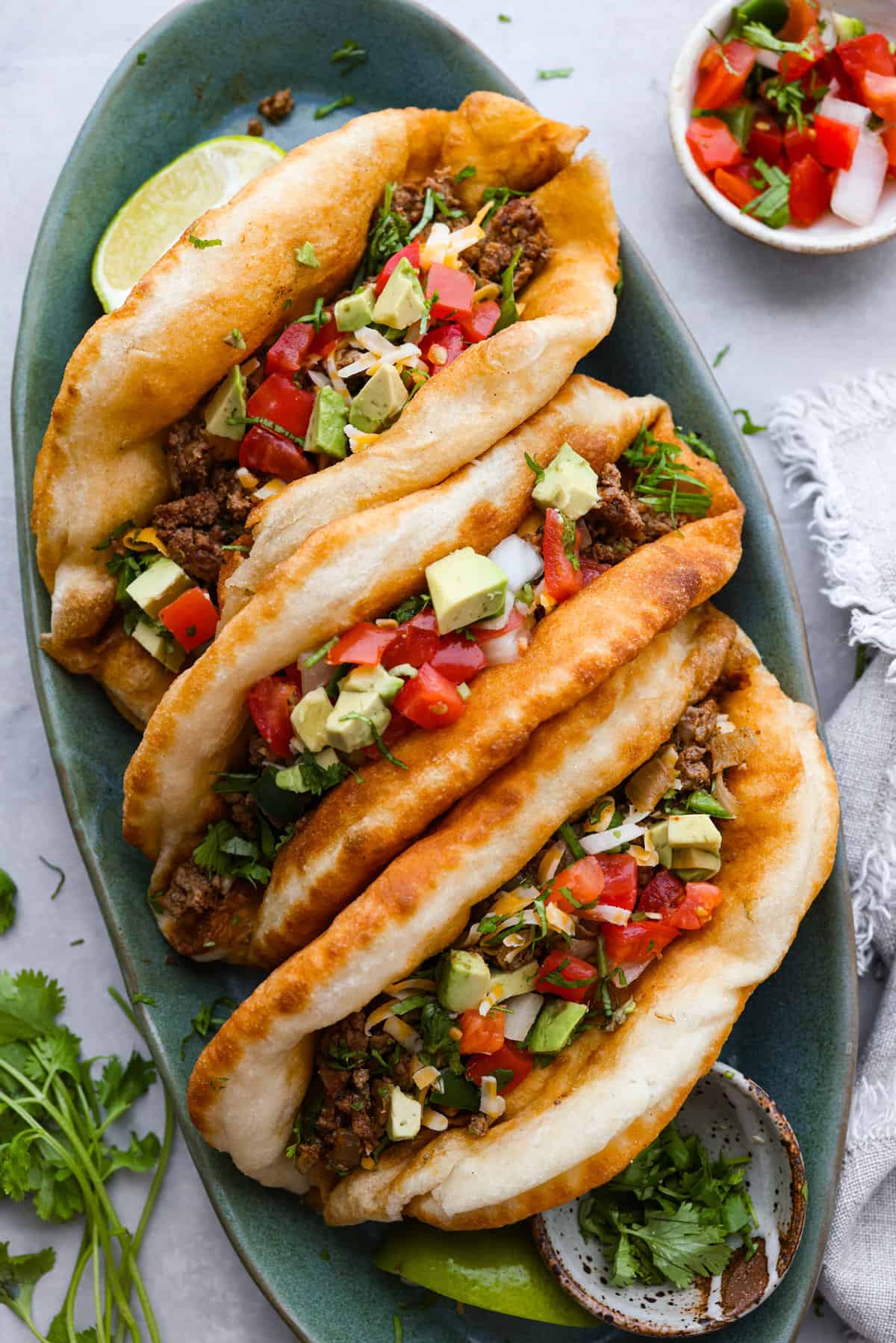 All your favorite taco fixings inside a warm, fluffy piece of fried bread! Homemade chalupas are a knockout dinner the whole family will go crazy over. 3 chalupas on a blue-green serving platter.