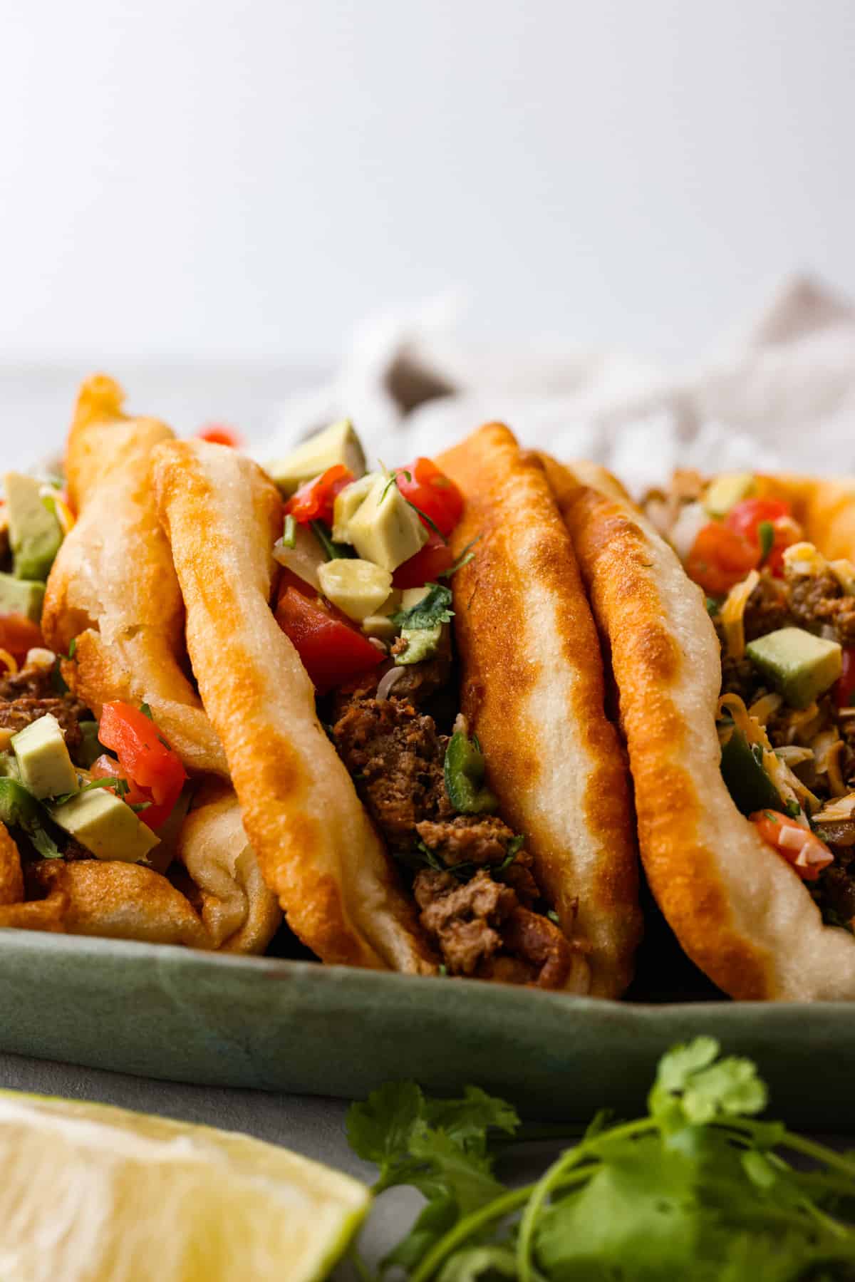 All your favorite taco fixings inside a warm, fluffy piece of fried bread! Homemade chalupas are a knockout dinner the whole family will go crazy over. Closeup of 3 chalupas filled with beef and vegetables.