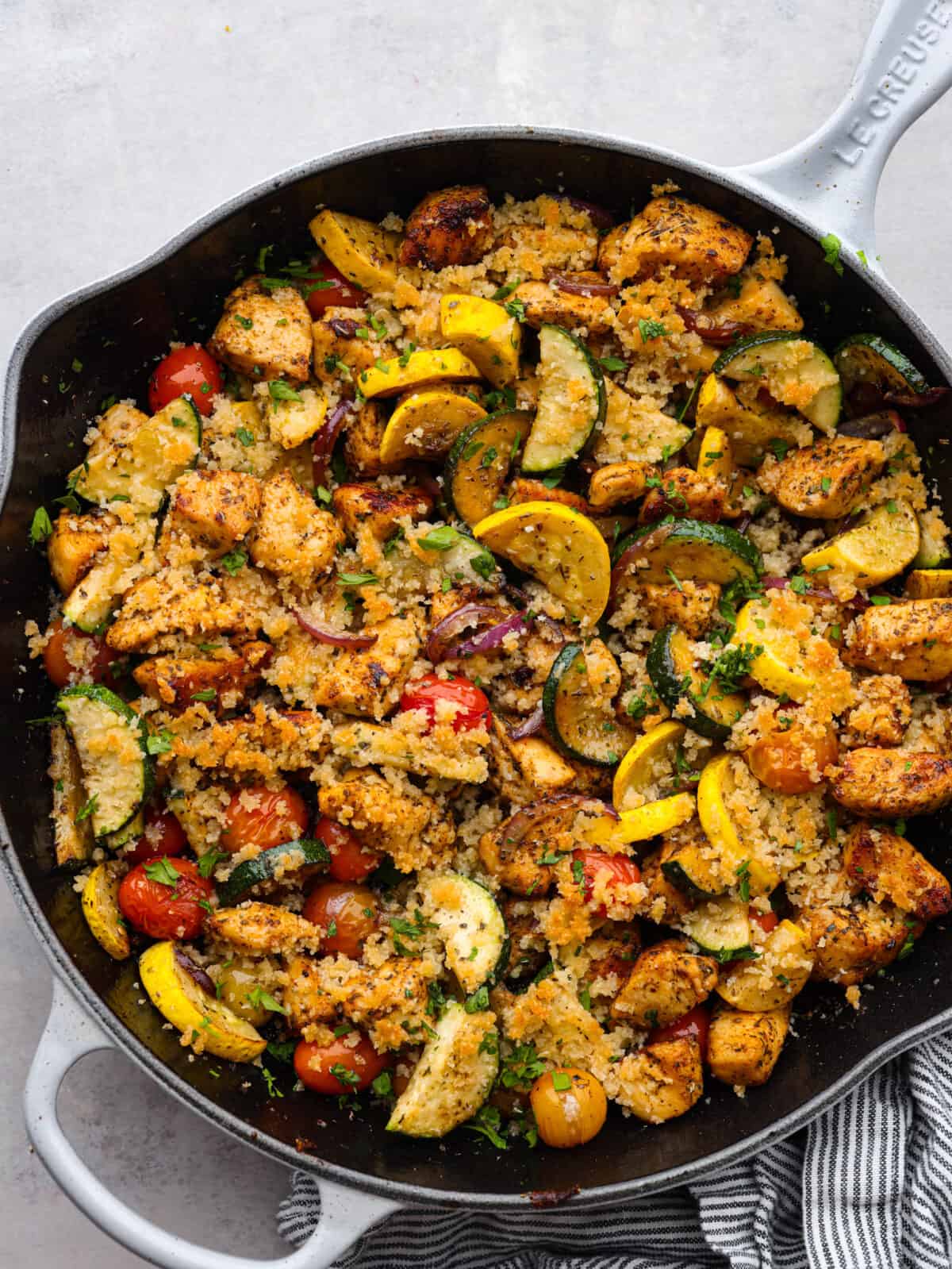 Use up all those garden veggies in this delicious chicken and garden vegetable skillet. Your family will love this healthy 30-minute skillet dinner full of seasoned chicken, sauteed vegetables, and a cheesy breadcrumb topping. Top view of chicken and garden vegetables in a black skillet.