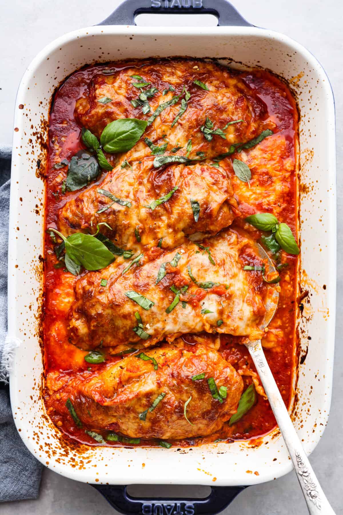 Herb-crusted chicken breasts coated in mozzarella, parmesan, and Italian seasoning, all smothered in homemade marinara sauce. Baked chicken marinara is simple, comforting, and oh-so-delicious! Top-down view of 4 chicken breasts coated in marinara sauce and cheese.
