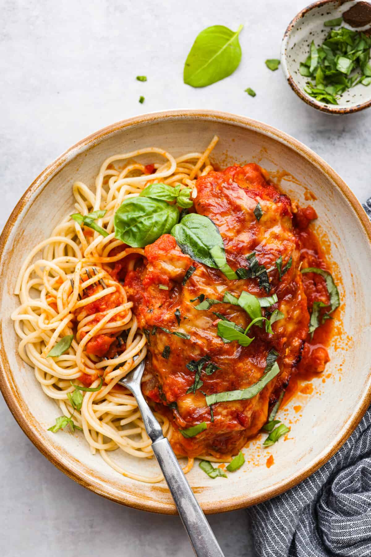Herb-crusted chicken breasts coated in mozzarella, parmesan, and Italian seasoning, all smothered in homemade marinara sauce. Baked chicken marinara is simple, comforting, and oh-so-delicious! Chicken served with spaghetti noodles and fresh basil.