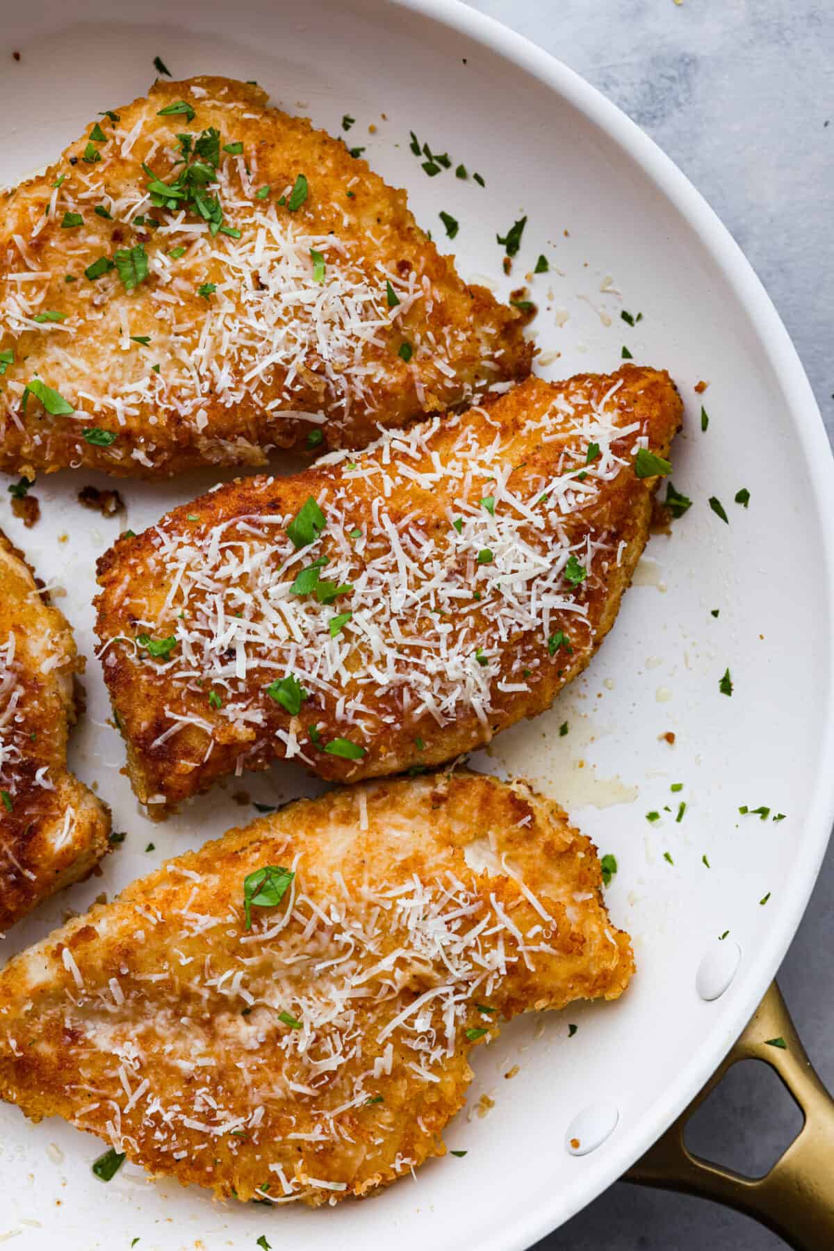 Romano-crusted chicken filets served with tangy marinara and spaghetti noodles. Chicken Romano is golden, crispy, flavorful, and sure to be your family's new favorite meal. Closeup of cooked chicken romano in a white skillet.