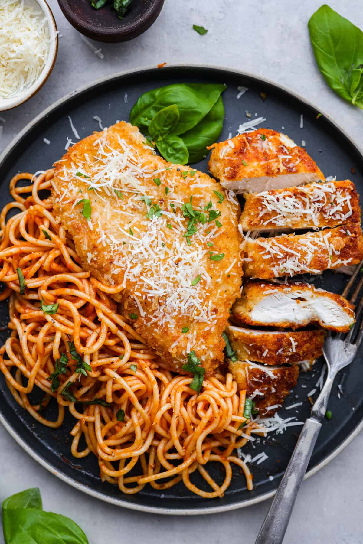 Romano-crusted chicken filets served with tangy marinara and spaghetti noodles. Chicken Romano is golden, crispy, flavorful, and sure to be your family's new favorite meal. Chicken romano served on a dark blue plate with spaghetti noodles.