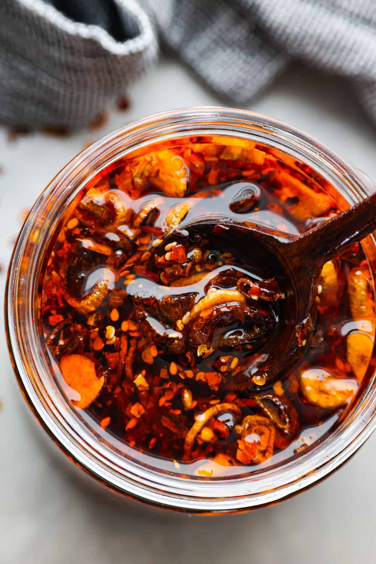 Chili crisp is the secret ingredient every kitchen needs to spice up your dishes effortlessly. It's a mix of crispy shallots, garlic, ginger, fiery chili flakes and sesame seeds that will add the best flavor to any dish! Top-down view of chili crisp oil in a glass jar.