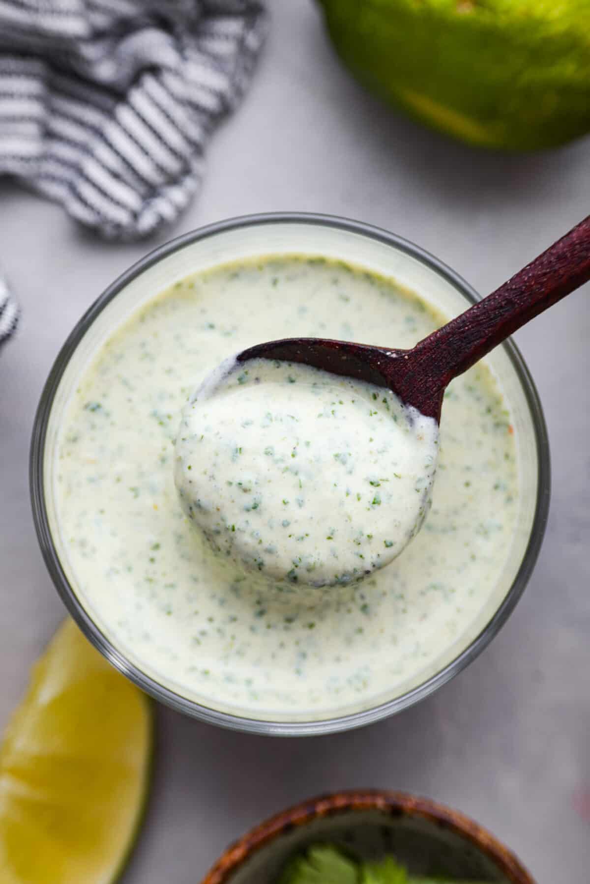 Once you taste this creamy cilantro lime sauce, you'll want to drizzle it on everything in sight! It's a tasty mix of sour cream, cilantro, salsa verde, lime juice, garlic, salt, and pepper. Perfect for grilled meats, salads, tacos, and more! Top-down view of cilantro lime sauce.