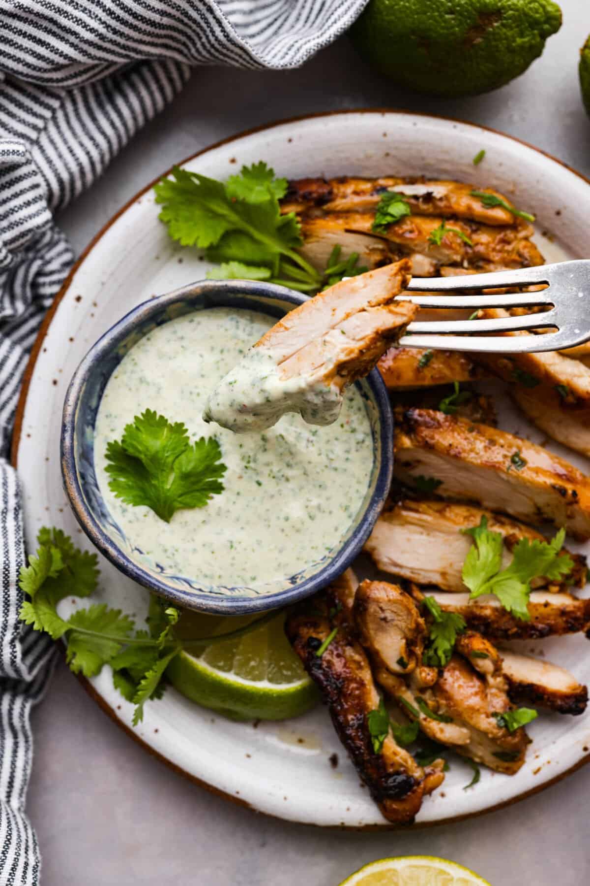 Once you taste this creamy cilantro lime sauce, you'll want to drizzle it on everything in sight! It's a tasty mix of sour cream, cilantro, salsa verde, lime juice, garlic, salt, and pepper. Perfect for grilled meats, salads, tacos, and more! Cilantro sauce served with sliced chicken.