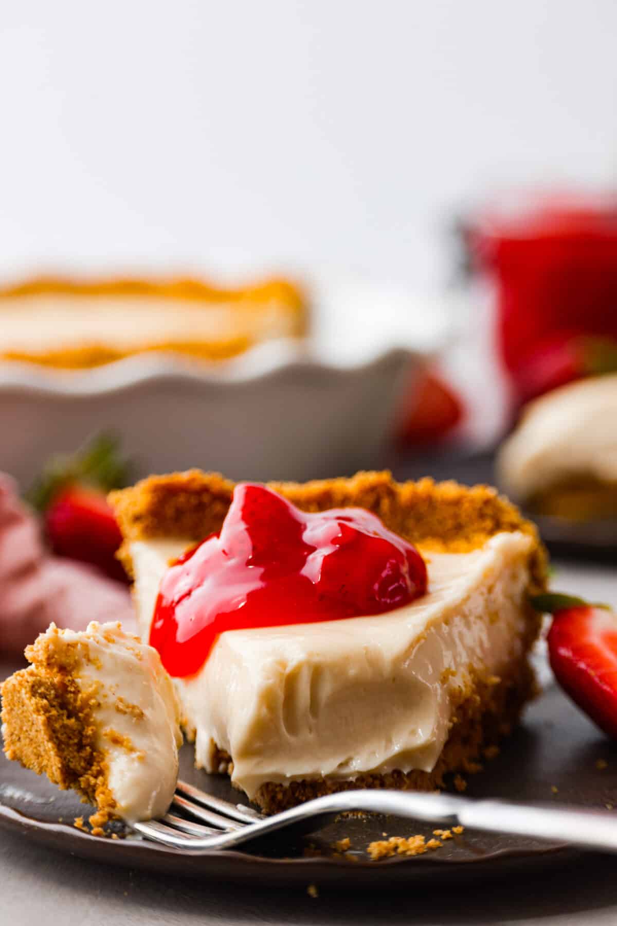 Experience pure dessert delight with this Cream Cheese Pie! A buttery graham cracker crust with a smooth cream cheese filling, and just a touch of lemon and vanilla. It's so easy and simply delicious. A slice of cream cheese pie with a dollop of strawberry pie filling on top.