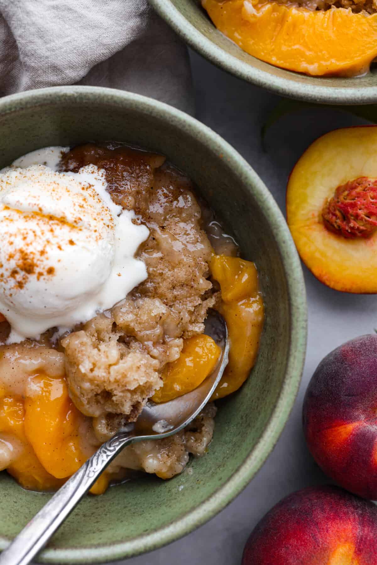 This Slow Cooker Peach Cobbler is an easy dessert, perfect for those fresh summer peaches! It has a sweet biscuit topping and deliciously sweet peach filling underneath that is perfect when served with a scoop of vanilla ice cream. A close up of a bowl of slow cooker peach cobbler.