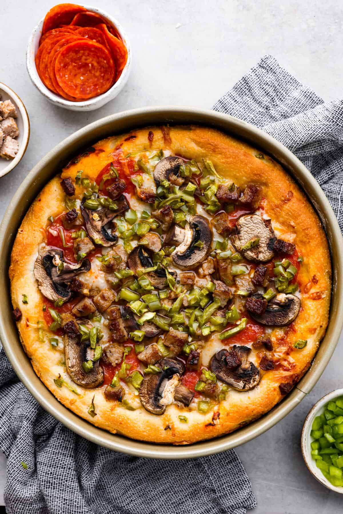 Authentic Chicago-style deep dish pizza! A thick, crispy and flaky crust topped with an easy homemade marinara sauce and shredded mozzarella cheese! It's comfort food at its finest and something the whole family will love. Top-down view of deep dish pizza topped with pepperoni, peppers, and mushrooms.