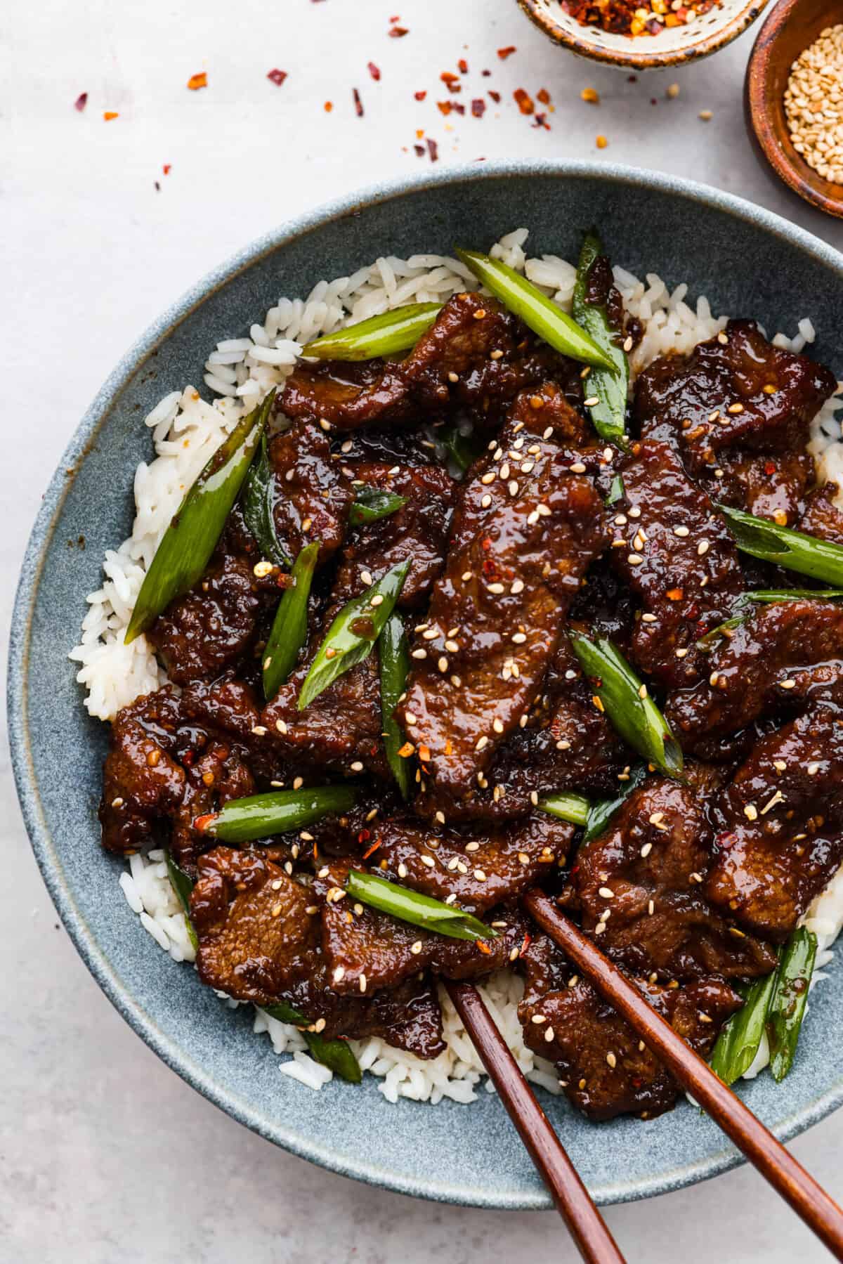 This Mongolian beef is crazy tender with a crispy seared edge that gets coated in a bold sticky sauce. It's way better than P.F. Changs and so easy to make at home! Mongolian beef served over rice in a blue bowl.