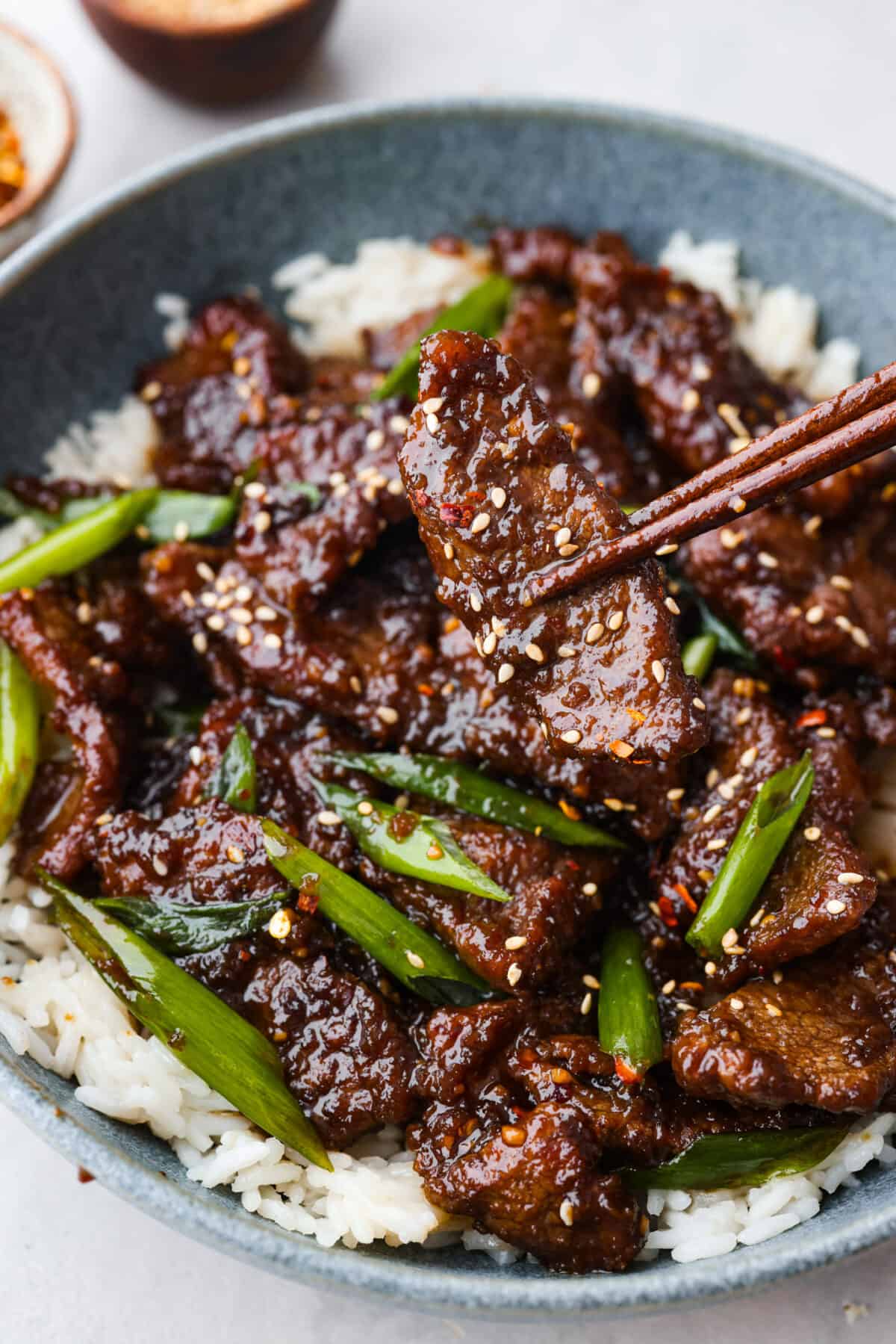 This Mongolian beef is crazy tender with a crispy seared edge that gets coated in a bold sticky sauce. It's way better than P.F. Changs and so easy to make at home! Picking up a piece of Mongolian beef with chopsticks.