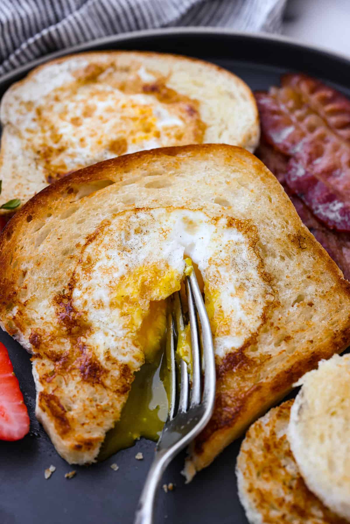 The ultimate all-in-one breakfast, here is how you can make the best "egg in a hole!" This easy dish is all about that crispy, buttery toast hugging those perfectly fried eggs. It's the most simple and delicious way to start off your morning! Breaking the yolk of the egg so it becomes runny.