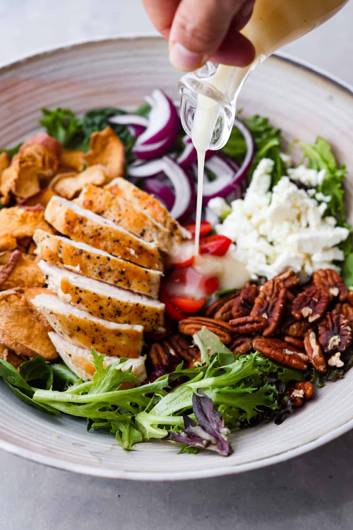 Spring greens get tossed with crisp apples, chicken, tomatoes, dried cranberries, crunchy pecans and feta cheese. This Panera Bread copycat Fuji apple chicken salad is a must-try! It's fresh, flavorful, and completely irresistible. Pouring the vinaigrette over the fuji apple chicken salad.