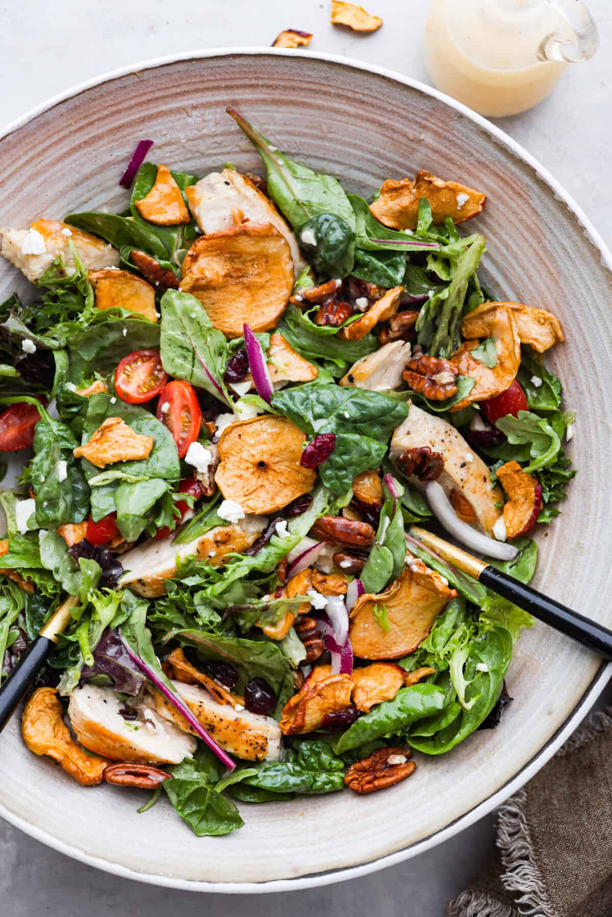 Spring greens get tossed with crisp apples, chicken, tomatoes, dried cranberries, crunchy pecans and feta cheese. This Panera Bread copycat Fuji apple chicken salad is a must-try! It's fresh, flavorful, and completely irresistible. Top-down view of salad with chicken, greens, tomatoes, apples, nuts, and feta cheese in a stoneware bowl.