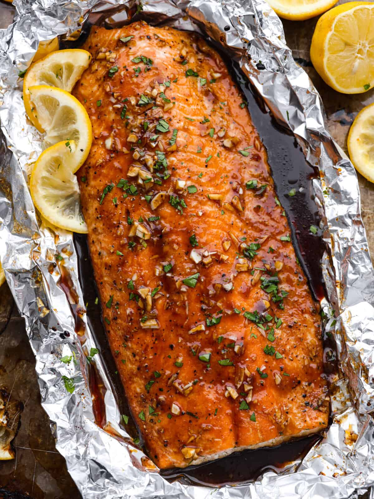 Garlic Brown Sugar Glazed Salmon is tender and flaky salmon covered in the most amazing garlic brown sugar soy glaze. The flavor is out of this world, and it will become a new family favorite! Salmon wrapped in foil and garnished with lemon slices.