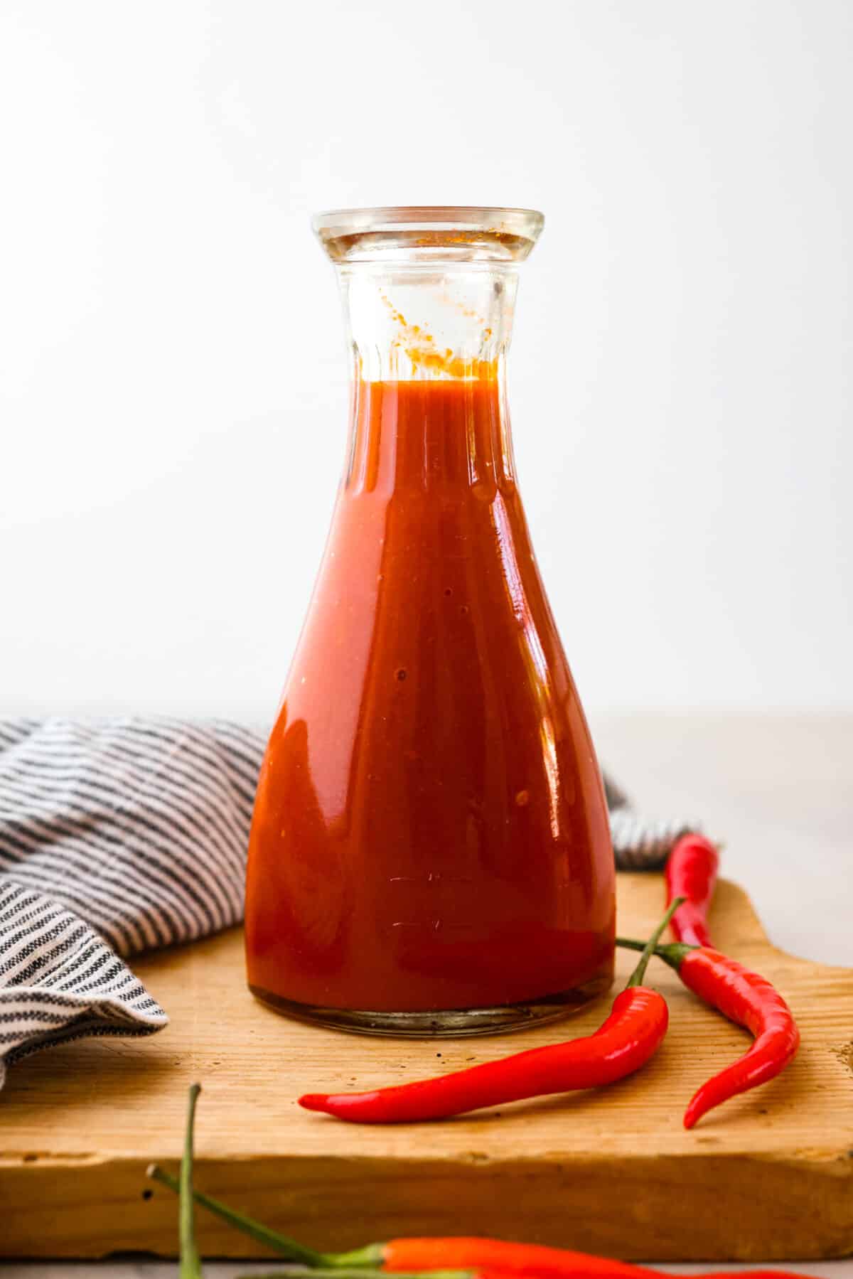 Sriracha sauce is a popular condiment that adds a burst of delicious spice to any dish. Try making it from scratch so it tastes just the way you like it! Homemade sriracha sauce in a glass bottle.